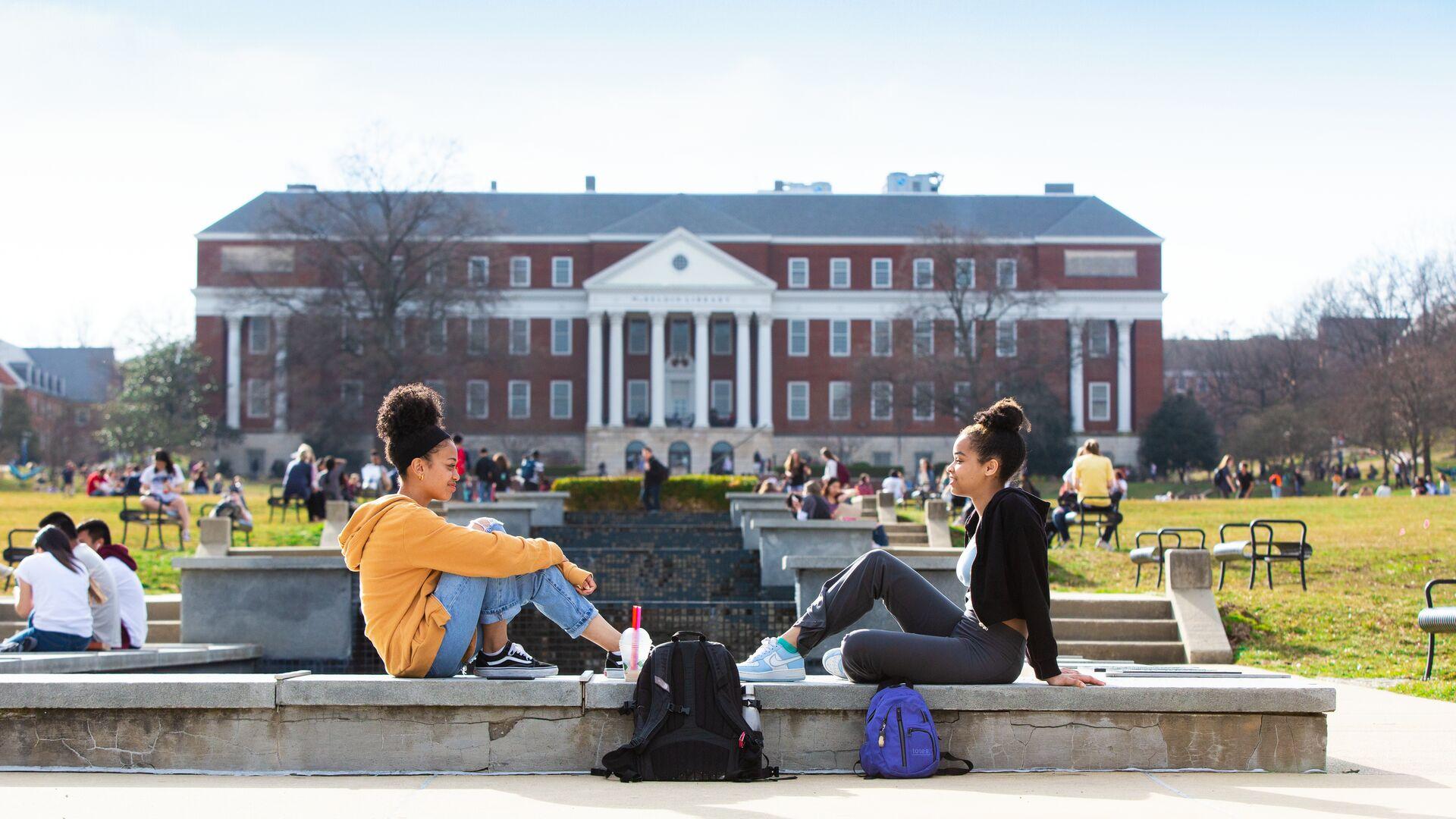 Two female students sitting along ODK Fountain with McKeldin Library in the background.